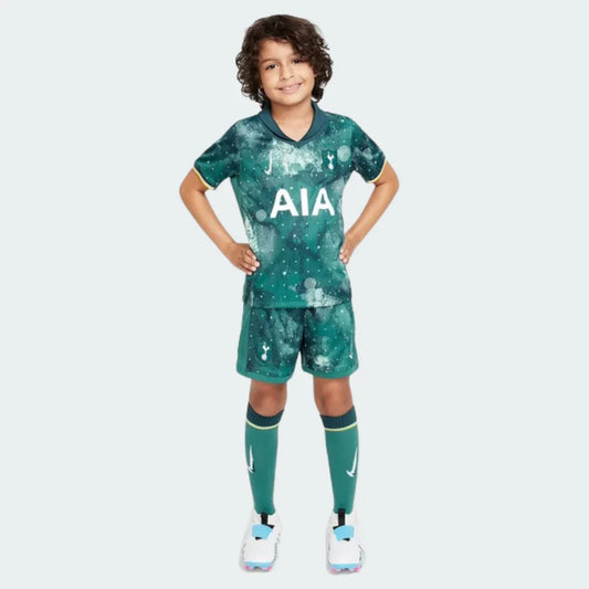 Menino vestindo kit infantil do Tottenham, com camisa e calção verde escuro estampa galáxia e meiões verdes.