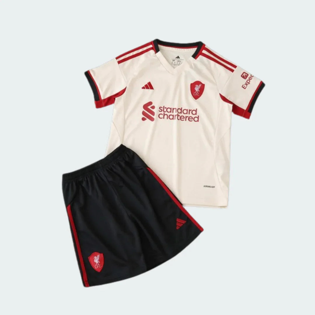 Kit infantil Liverpool 25/26, camisa creme com listras e emblemas vermelhos, shorts preto com detalhes vermelhos.