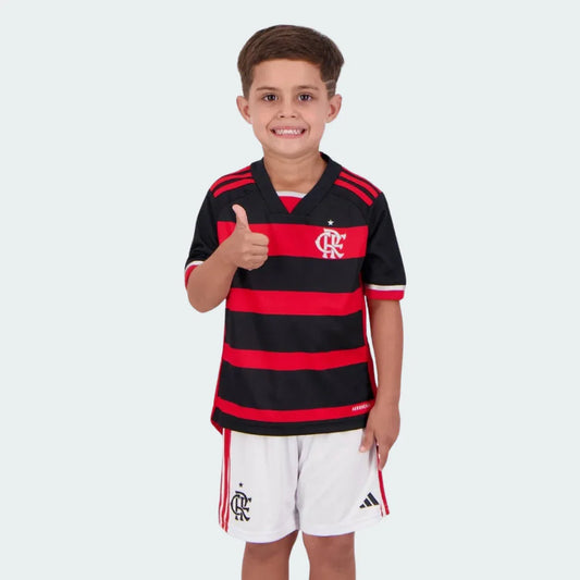 Menino sorridente de camiseta listrada preta e vermelha do Flamengo e shorts brancos, com símbolo CRF e logo Adidas, fazendo sinal de positivo.