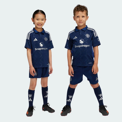 Duas crianças vestindo o kit infantil do Manchester United em azul escuro com detalhes em branco e calção azul.