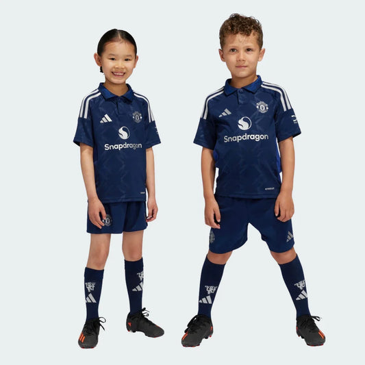 Duas crianças vestindo o kit infantil do Manchester United em azul escuro com detalhes em branco e calção azul.