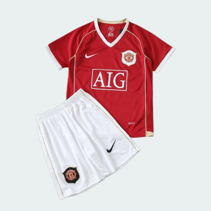 Kit infantil de futebol Manchester United. Camisa vermelha com logo AIG, escudo do time e Nike. Shorts brancos com escudo e logo Nike.