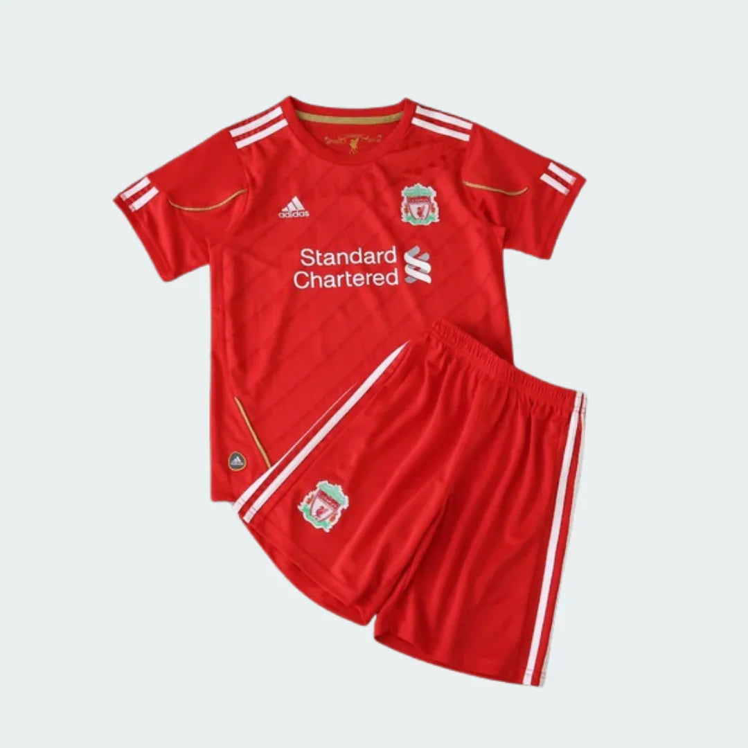 Kit infantil vermelho do Liverpool com camisa e shorts, ambos com escudo do time. Camisa com logo Adidas e patrocinador Standard Chartered.