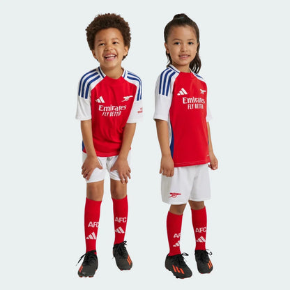 Dois sorridentes crianças, um menino e uma menina, vestindo o kit infantil do Arsenal. Camisas vermelhas, shorts brancos e meias vermelhas.