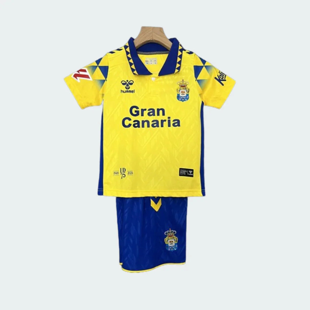 Foto de kit infantil Las Palmas I 24/25. Camisa amarela com gola azul, shorts azuis, logos Hummel e escudo do time.