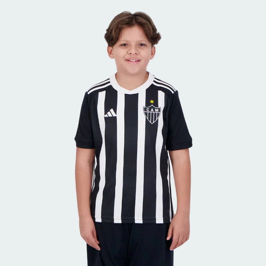 Menino sorrindo veste camisa oficial do Galo I 24/25 preta e branca listrada com escudo CAM, estrela amarela e shorts escuros.
