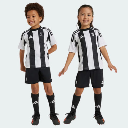 Dois crianças, um menino e uma menina, sorrindo e usando o kit infantil Juventus preto e branco, com shorts e meias pretos.
