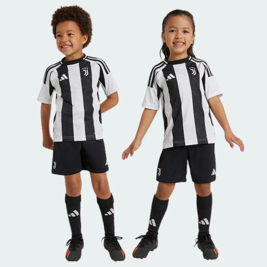 Dois crianças, um menino e uma menina, sorrindo e usando o kit infantil Juventus preto e branco, com shorts e meias pretos.
