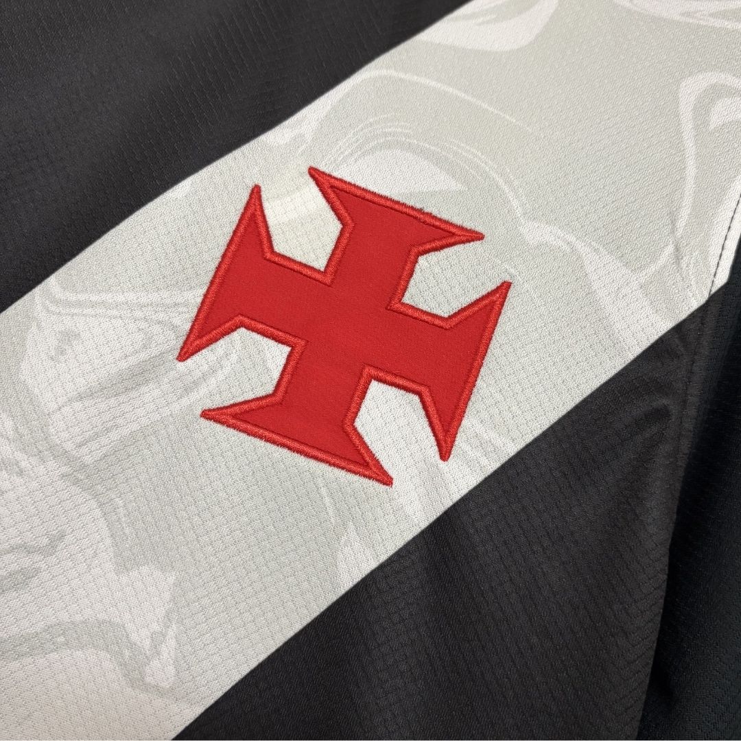 Close detalhado da Cruz de Malta em vermelho aplicada sobre a faixa diagonal branca, que apresenta grafismos sublimados em marca d'água no tecido.