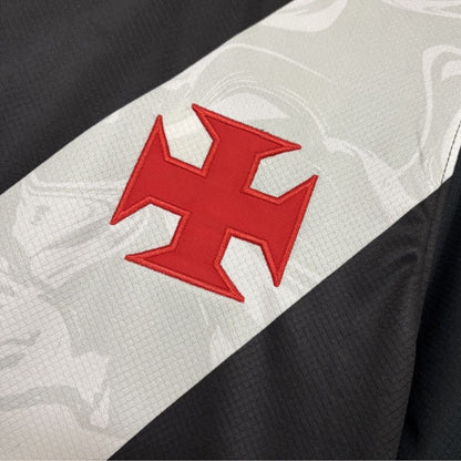 Close detalhado da Cruz de Malta em vermelho aplicada sobre a faixa diagonal branca, que apresenta grafismos sublimados em marca d'água no tecido.