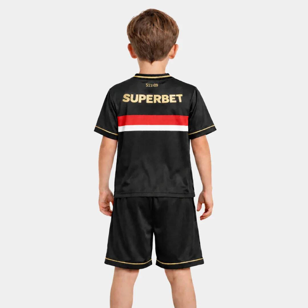 Visão traseira de um menino vestindo o kit completo, destacando a continuidade da faixa tricolor nas costas da camisa preta e o patrocínio "SUPERBET" em letras douradas na parte superior.