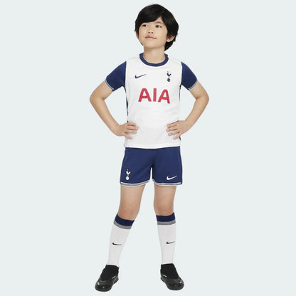Menino sorridente vestindo o Kit Infantil Tottenham I 24/25 branco e azul. Camisa branca, shorts azul e meias brancas.