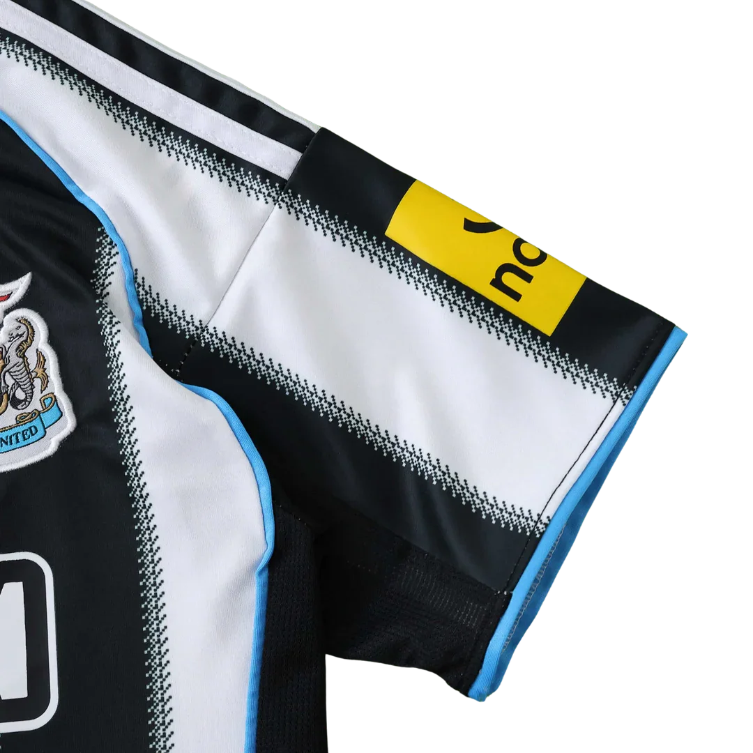 Detalhe da camisa infantil do Newcastle United, listrada em preto e branco, com escudo, detalhes azuis e logo na manga.