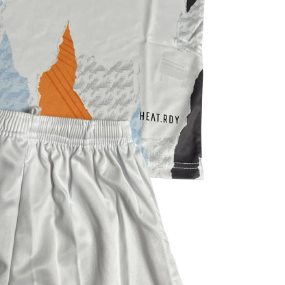 Kit de futebol infantil branco com camisa de estampa abstrata laranja, azul e cinza, e shorts brancos. Detalhe HEAT.RDY visível.