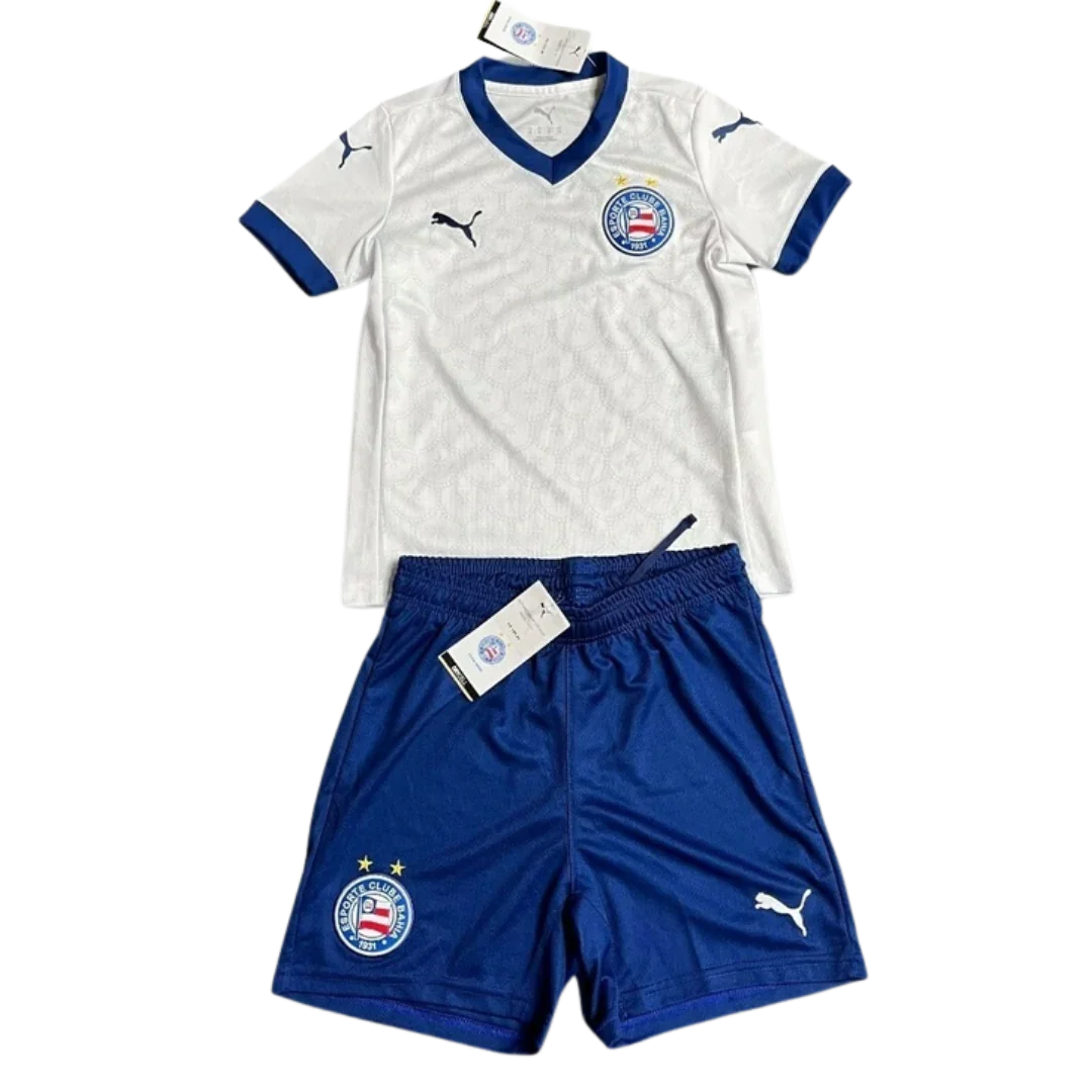 Kit infantil Bahia I 25/26, camisa branca de gola V azul e shorts azul com escudos e logos Puma.
