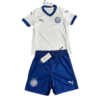 Kit infantil Bahia I 25/26, camisa branca de gola V azul e shorts azul com escudos e logos Puma.