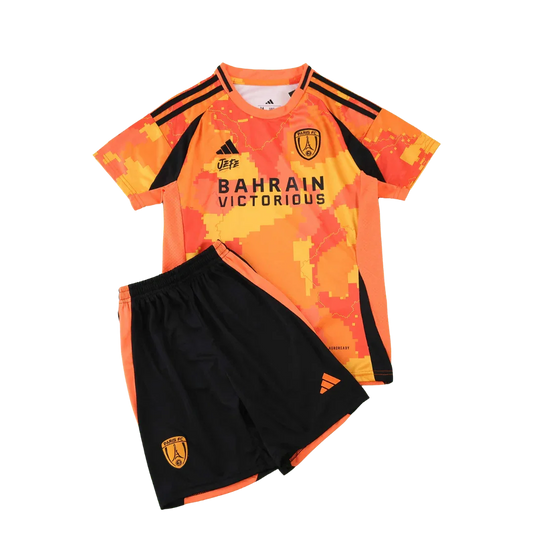 Kit infantil Paris FC 25/26 com camisa laranja pixelada e shorts pretos. Detalhes em preto e laranja. Escudos do time e patrocinadores visíveis.