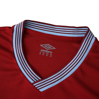Close-up da gola V de uma camisa de futebol infantil Umbro na cor vinho com detalhes listrados em azul claro e vinho.