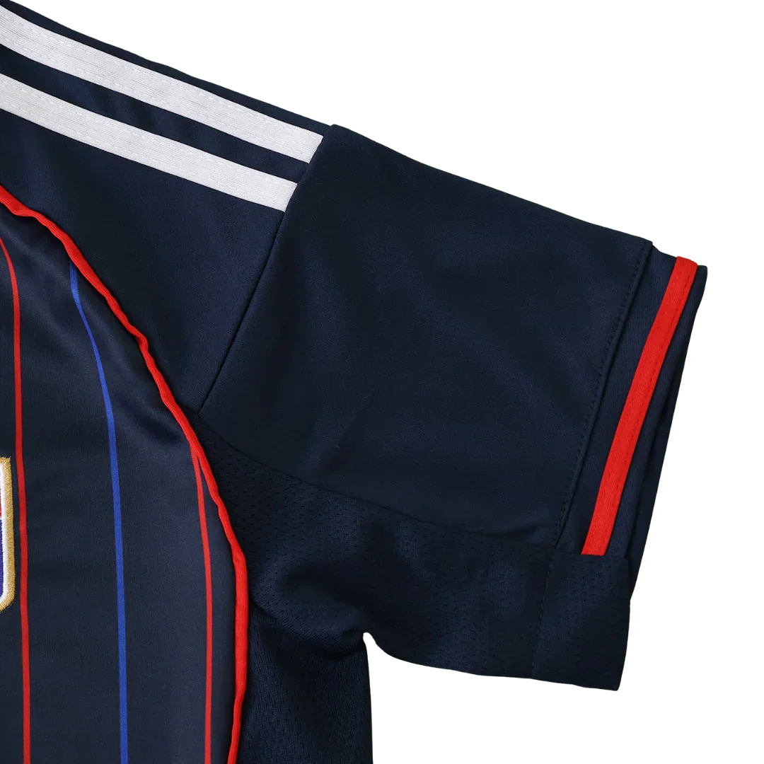 Close-up de camisa de futebol infantil azul escura: ombro com 3 listras brancas, listras verticais vermelhas e azuis no corpo, e faixa vermelha na manga.