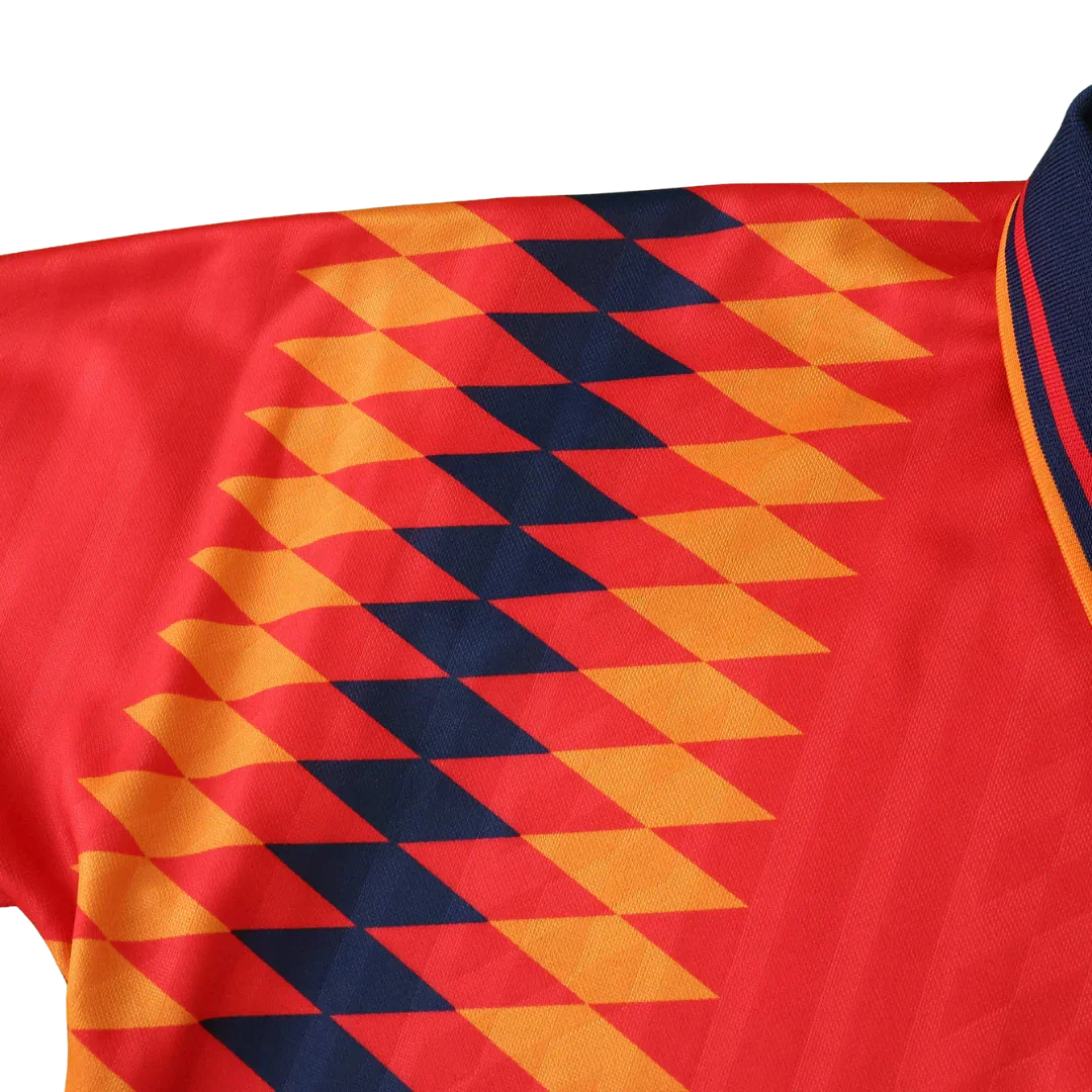 Detalhe da camisa de futebol infantil vermelha com padrão diagonal de losangos laranja e azul marinho, e gola azul escura listrada.