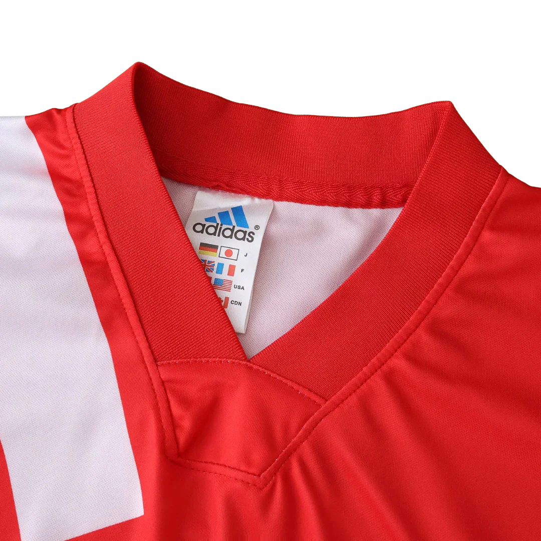 Foto detalhada de uma camisa de futebol infantil vermelha com gola V, listras brancas e etiqueta Adidas visível.