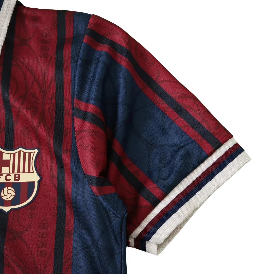 Close-up da camisa infantil do FC Barcelona com listras verticais vinho, azul marinho e pretas, e escudo dourado.
