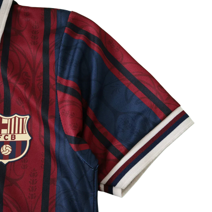 Close-up da camisa infantil do FC Barcelona com listras verticais vinho, azul marinho e pretas, e escudo dourado.