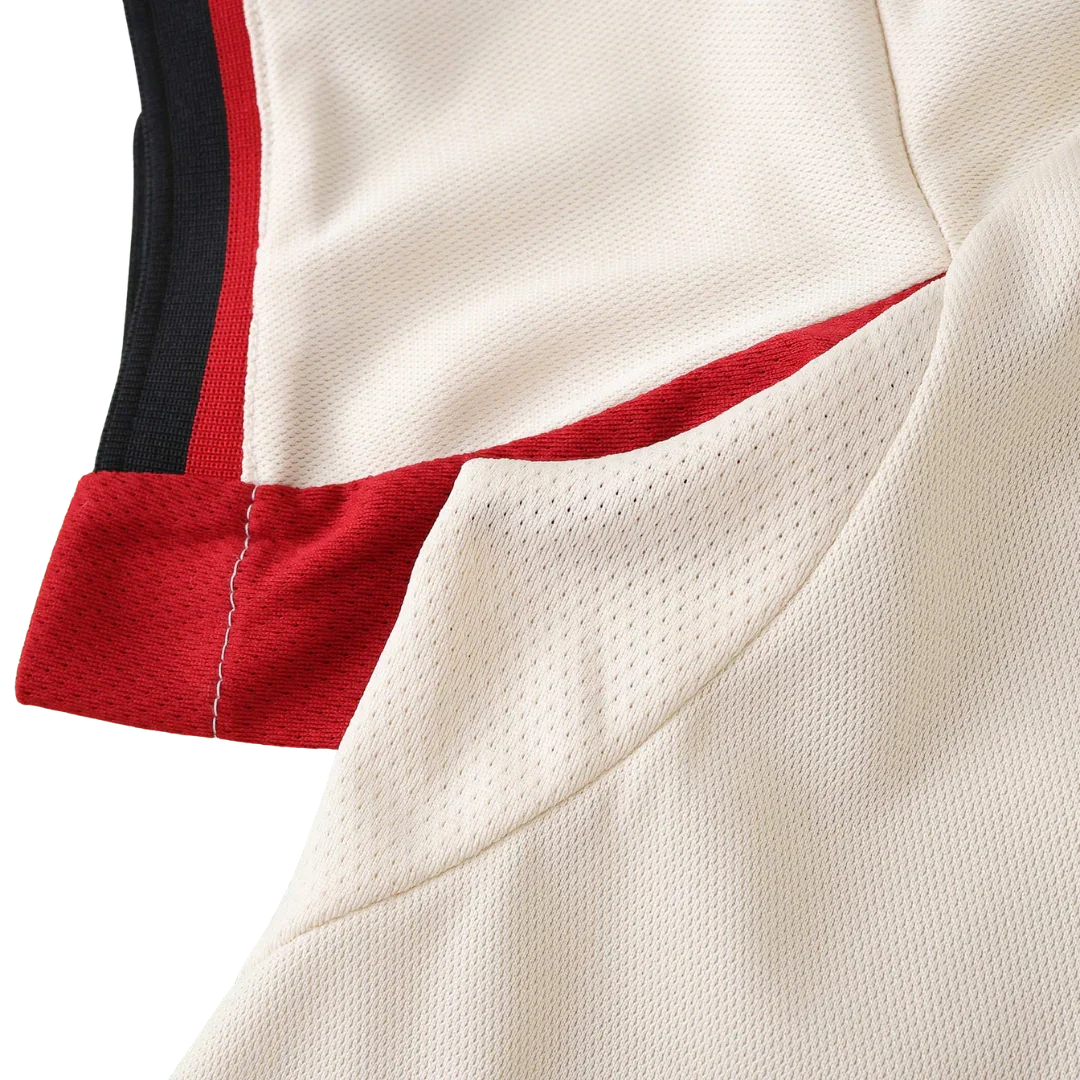 Detalhe da camisa de futebol infantil na cor creme, com painéis laterais em mesh, detalhes em vermelho e listras pretas.