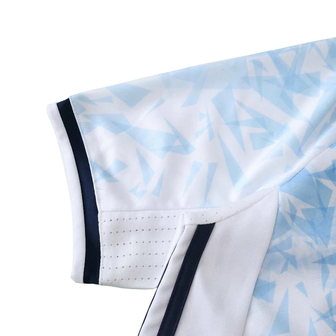 Detalhe da manga de uma camisa de futebol infantil branca com padrão geométrico azul claro, listras azul escuro e perfurações para ventilação.