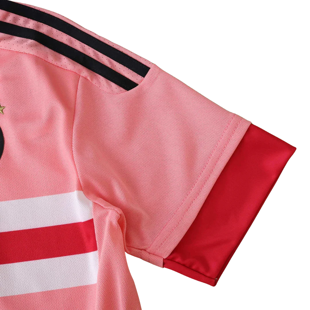 Foto aproximada da lateral de uma camisa de futebol infantil predominantemente rosa com listras pretas no ombro, listras horizontais brancas e vermelhas no corpo e punho vermelho.