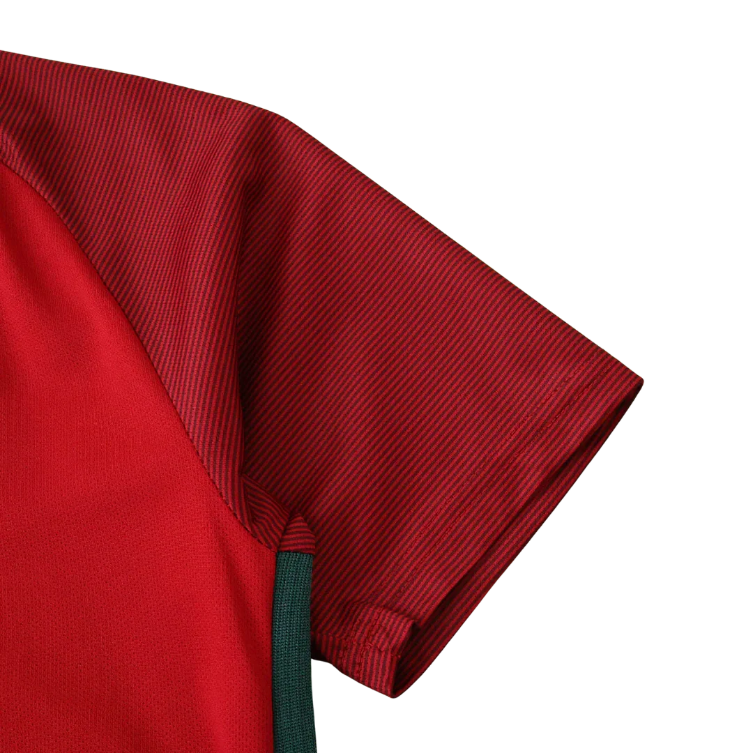 Detalhe da camisa de futebol infantil vermelha com manga listrada em tom escuro e detalhe lateral verde. Vista lateral do ombro.
