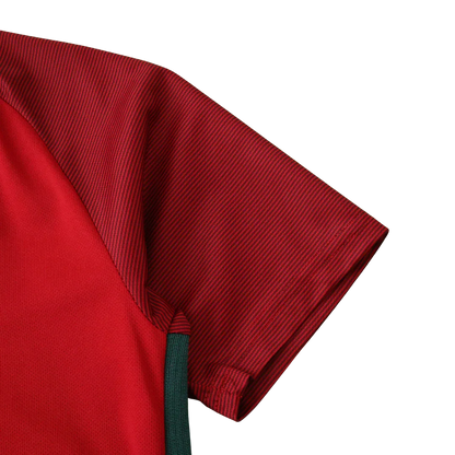 Detalhe da camisa de futebol infantil vermelha com manga listrada em tom escuro e detalhe lateral verde. Vista lateral do ombro.