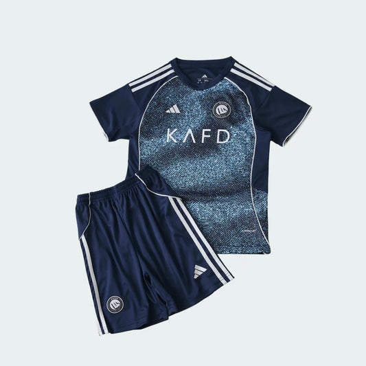 Kit infantil Al Nassr II 25/26 azul escuro, com camisa de estampa azul claro e shorts combinando, ambos com escudo e listras brancas.