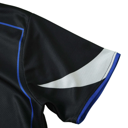 Manga de camisa infantil preta com detalhe branco e azul. Tecido texturizado e costura visível.