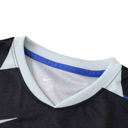 Close-up da gola V de uma camisa de futebol infantil preta, com gola cinza claro e faixa azul interna. Logo Nike e Dry-Fit visíveis.