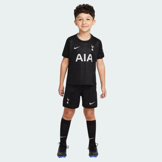 Menino sorridente em pé, vestindo o Kit Infantil Tottenham II 25/26 preto com logos brancos da Nike, AIA e escudo do Tottenham.