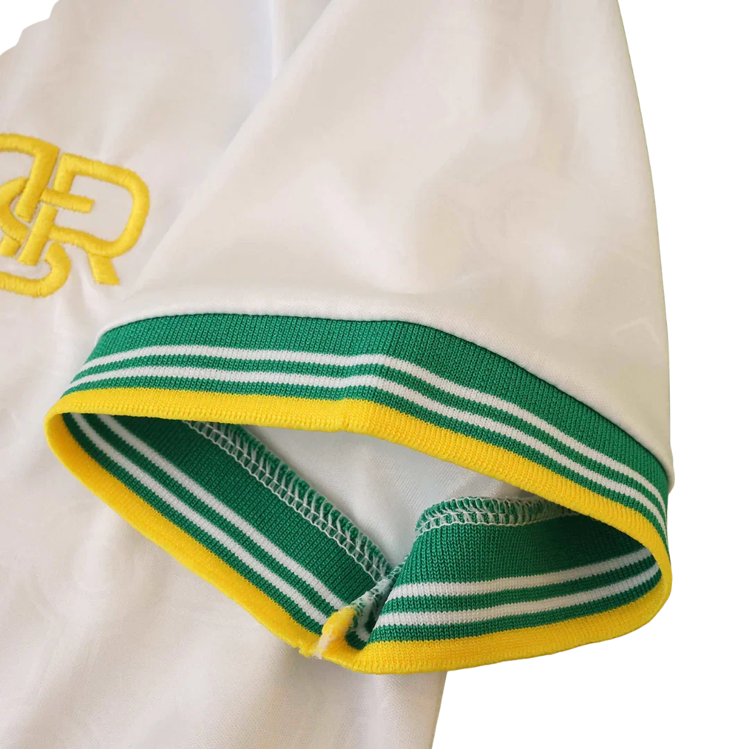 Manga de camisa infantil branca com punho listrado verde, branco e amarelo. Detalhe de bordado amarelo na camisa.