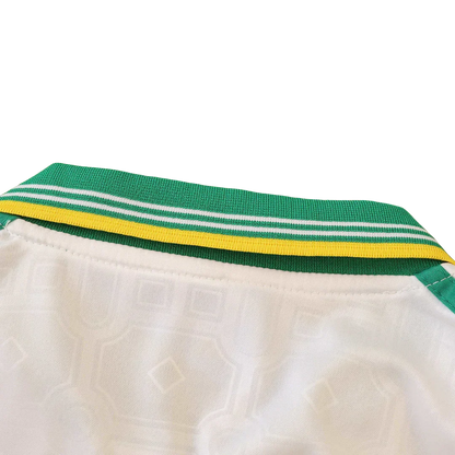 Detalhe da gola e parte superior de uma camisa de futebol infantil branca, com gola listrada em verde, branco e amarelo.