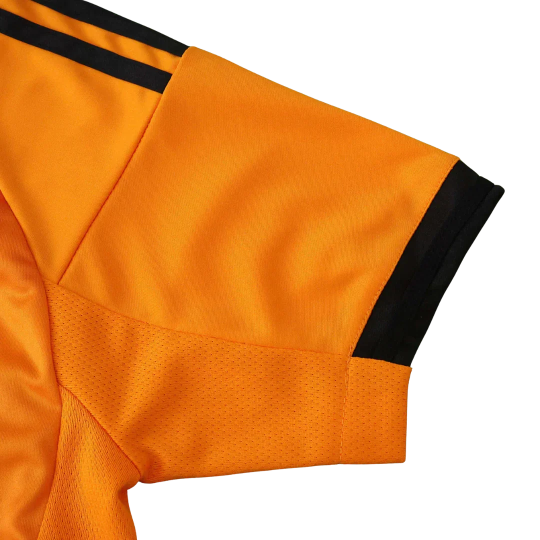 Detalhe da manga de uma camisa de futebol infantil laranja, com duas listras pretas no ombro, punho preto e painel de mesh na axila.