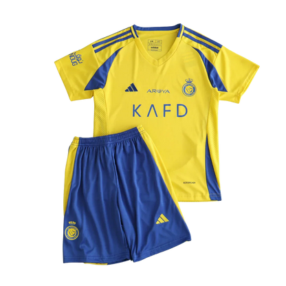 Kit infantil Al Nassr I 24/25 amarelo e azul com camisa de manga curta e shorts. Logos da Adidas, AROYA, KAFD e escudo do clube visíveis.