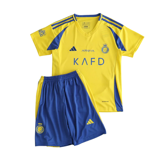 Kit infantil Al Nassr I 24/25 amarelo e azul com camisa de manga curta e shorts. Logos da Adidas, AROYA, KAFD e escudo do clube visíveis.