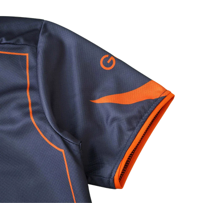 Close-up da manga de uma camisa de futebol infantil cinza escuro com detalhes laranja, incluindo um logo 'G' e barra. 