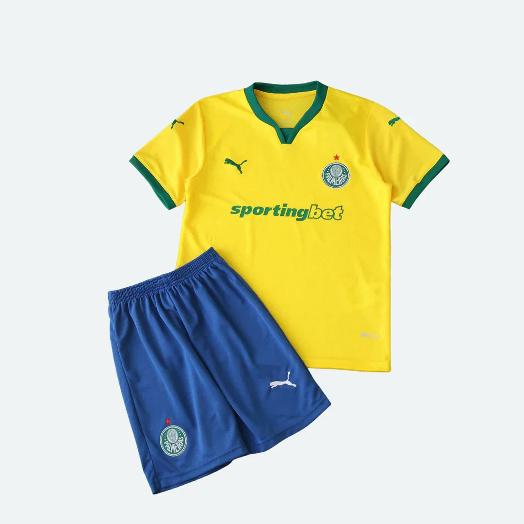 Kit de futebol infantil com camisa amarela de manga curta e shorts azul. Contém logo Puma e escudo redondo verde e branco.