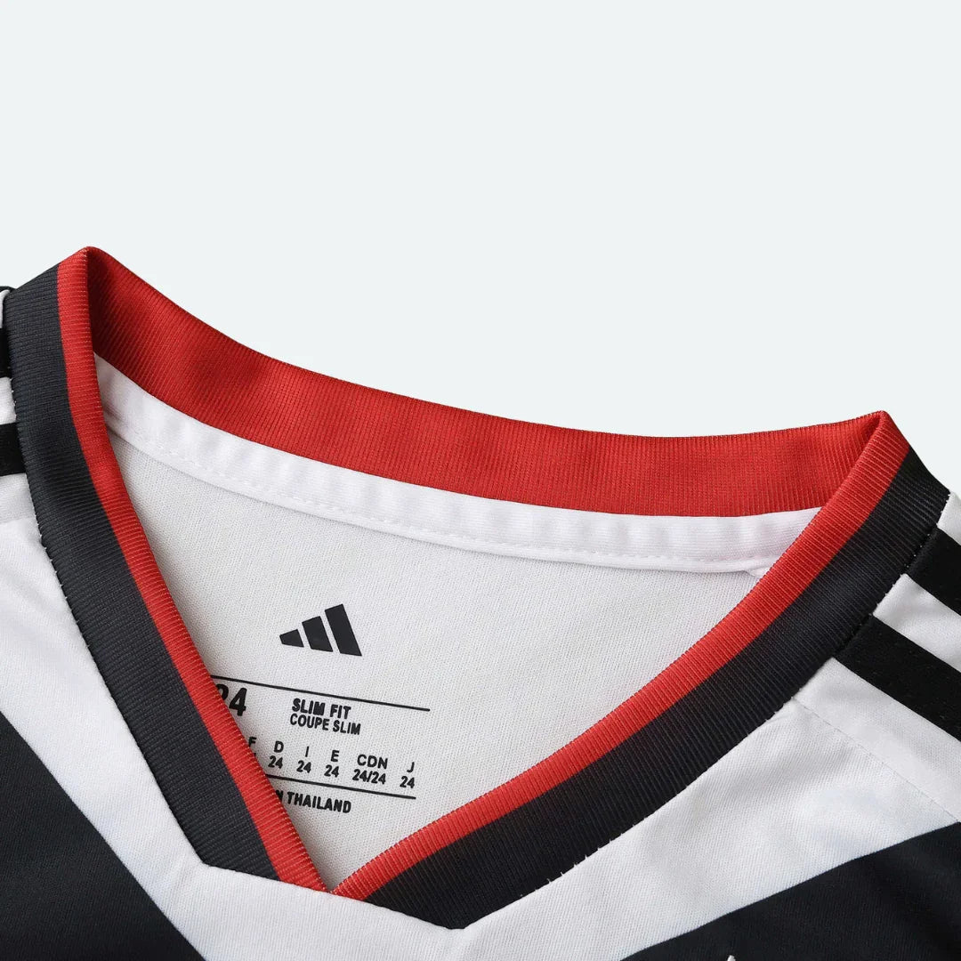 Detalhe do colarinho de camisa infantil branca com gola vermelha e preta, e etiqueta interna Adidas com 'SLIM FIT' e 'MADE IN THAILAND'.