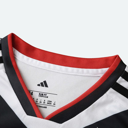 Detalhe do colarinho de camisa infantil branca com gola vermelha e preta, e etiqueta interna Adidas com 'SLIM FIT' e 'MADE IN THAILAND'.