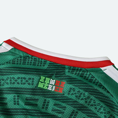 Detalhe da gola de uma camisa verde escura com detalhes gráficos e escrito 'SOMOS MÉXICO'.