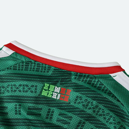 Detalhe da gola de uma camisa verde escura com detalhes gráficos e escrito 'SOMOS MÉXICO'.