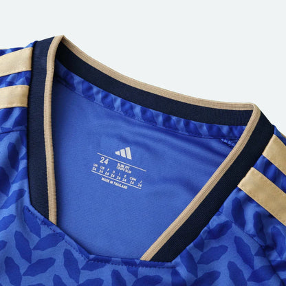 Close-up da etiqueta interna de uma camisa infantil azul com detalhes bege/dourado, tamanho 24.