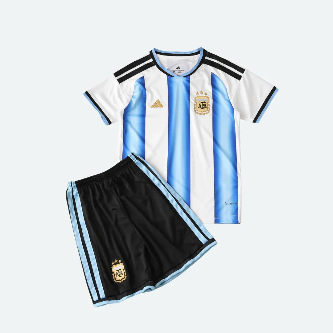 Kit infantil completo da Argentina. Camisa branca com listras azuis claras e shorts pretos com listras azuis claras, ambos com escudo AFA dourado.