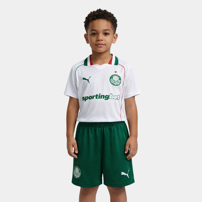 Menino vestindo o kit infantil do Palmeiras, com camisa branca, detalhes em verde e vermelho, e calção verde